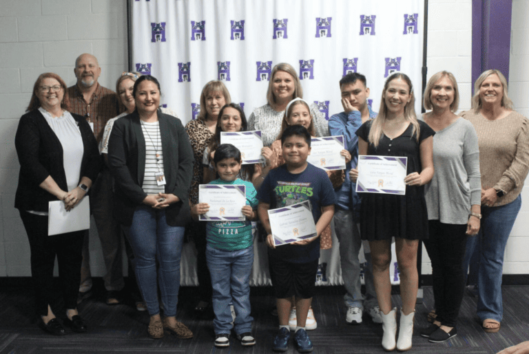 A diverse group of individuals proudly displaying their certificates in front of a vibrant purple wall.
