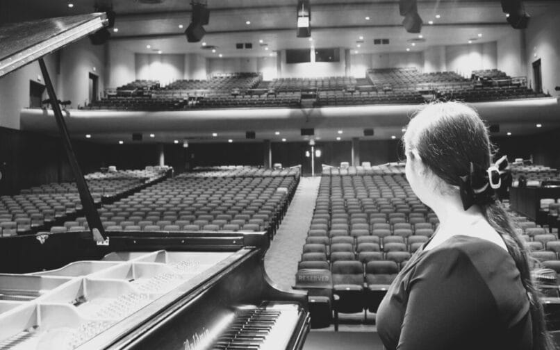 female student sitting at piano looking out at the auditorium