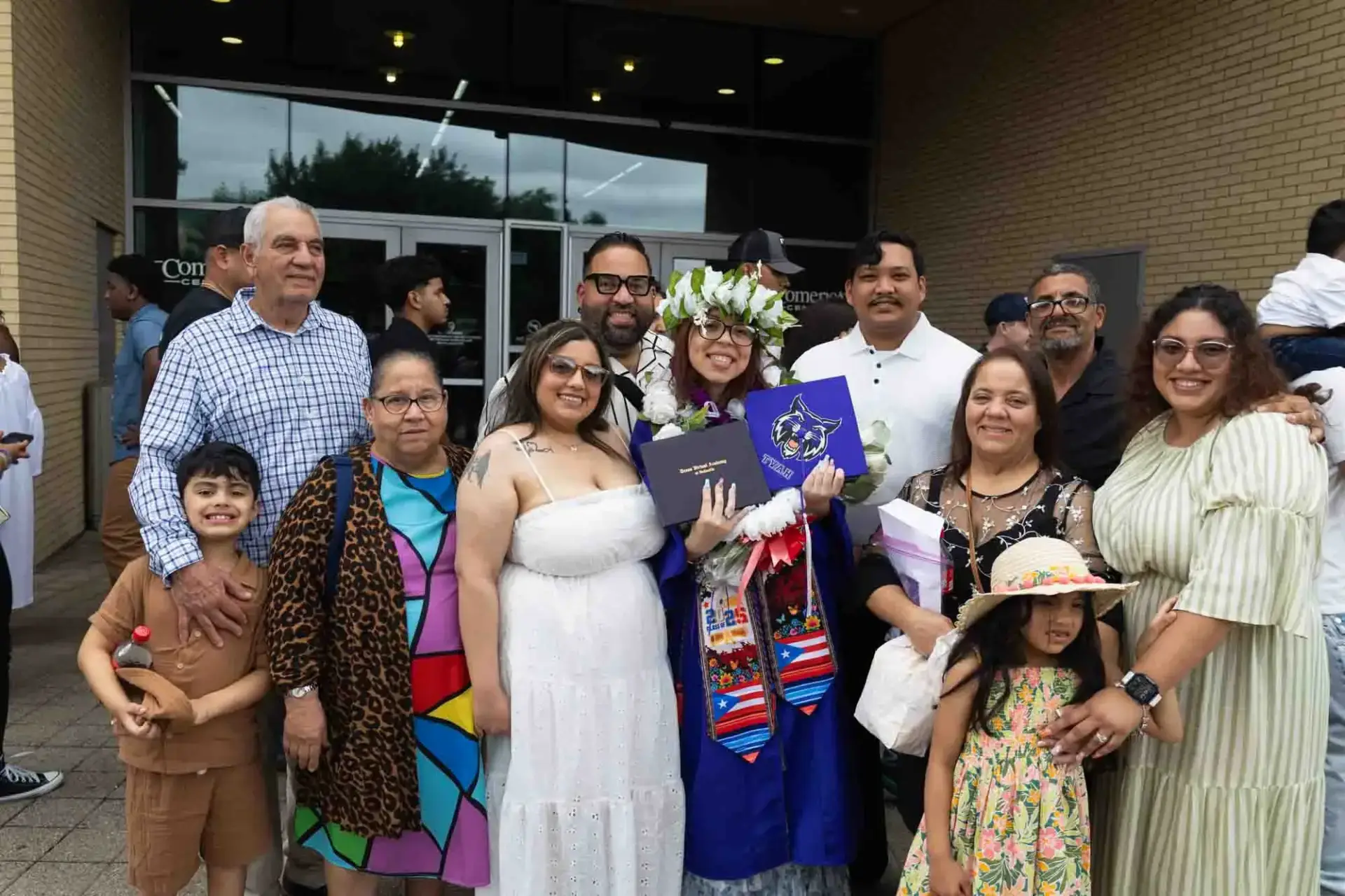 A joyful family gathers to celebrate a graduate in a blue cap and gown, holding diplomas. Smiles and colorful attire reflect pride and happiness.